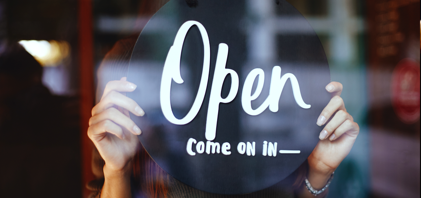 Hands holding up a drink tray that says 'Open, come on in-' through a clear, glass window.