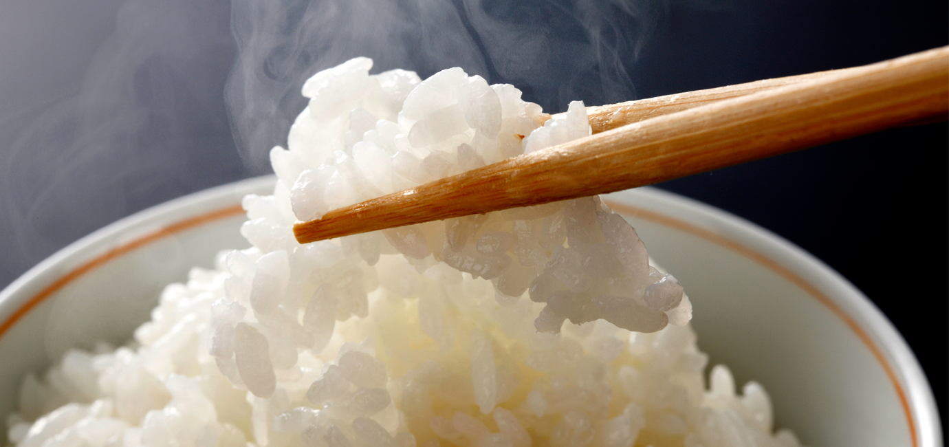 Chopsticks picking up steaming rice from a white bowl next to vertical Chinese calligraphy.