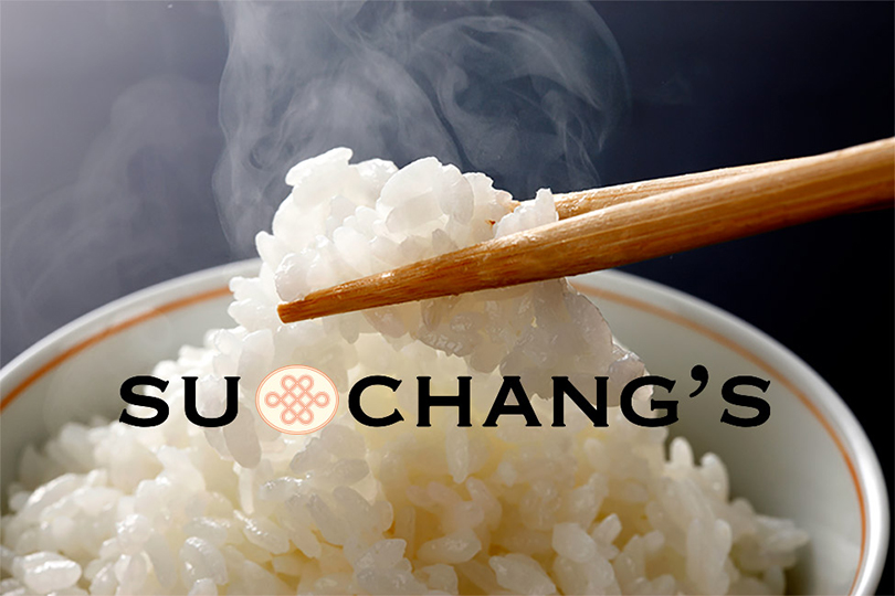 Chopsticks picking up steaming rice from a white bowl next to vertical Chinese calligraphy.